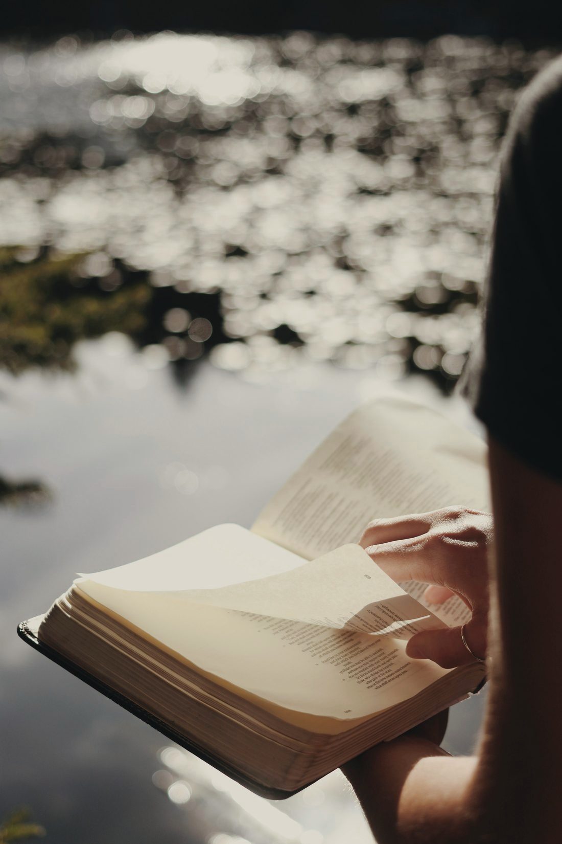 Hands holding an open Bible by a lake